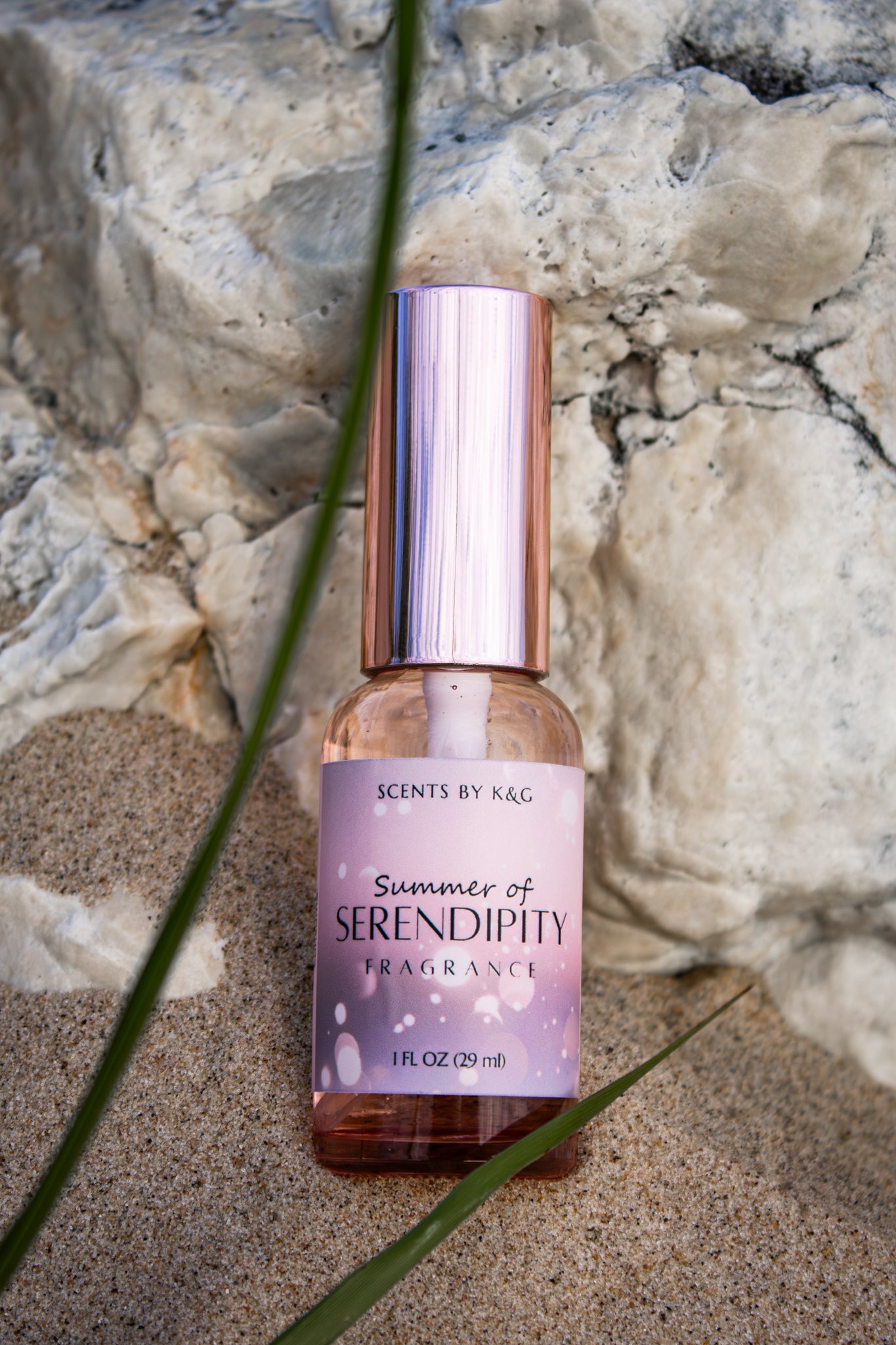 Fragrance bottle labeled 'Summer of Serendipity' on a beach with a rock background and dune grass.