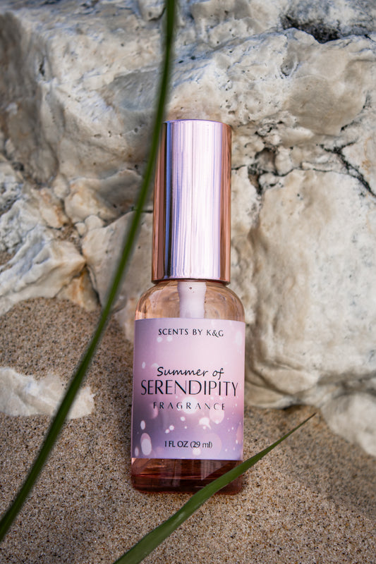 Fragrance bottle labeled 'Summer of Serendipity' on a beach with a rock background and dune grass.