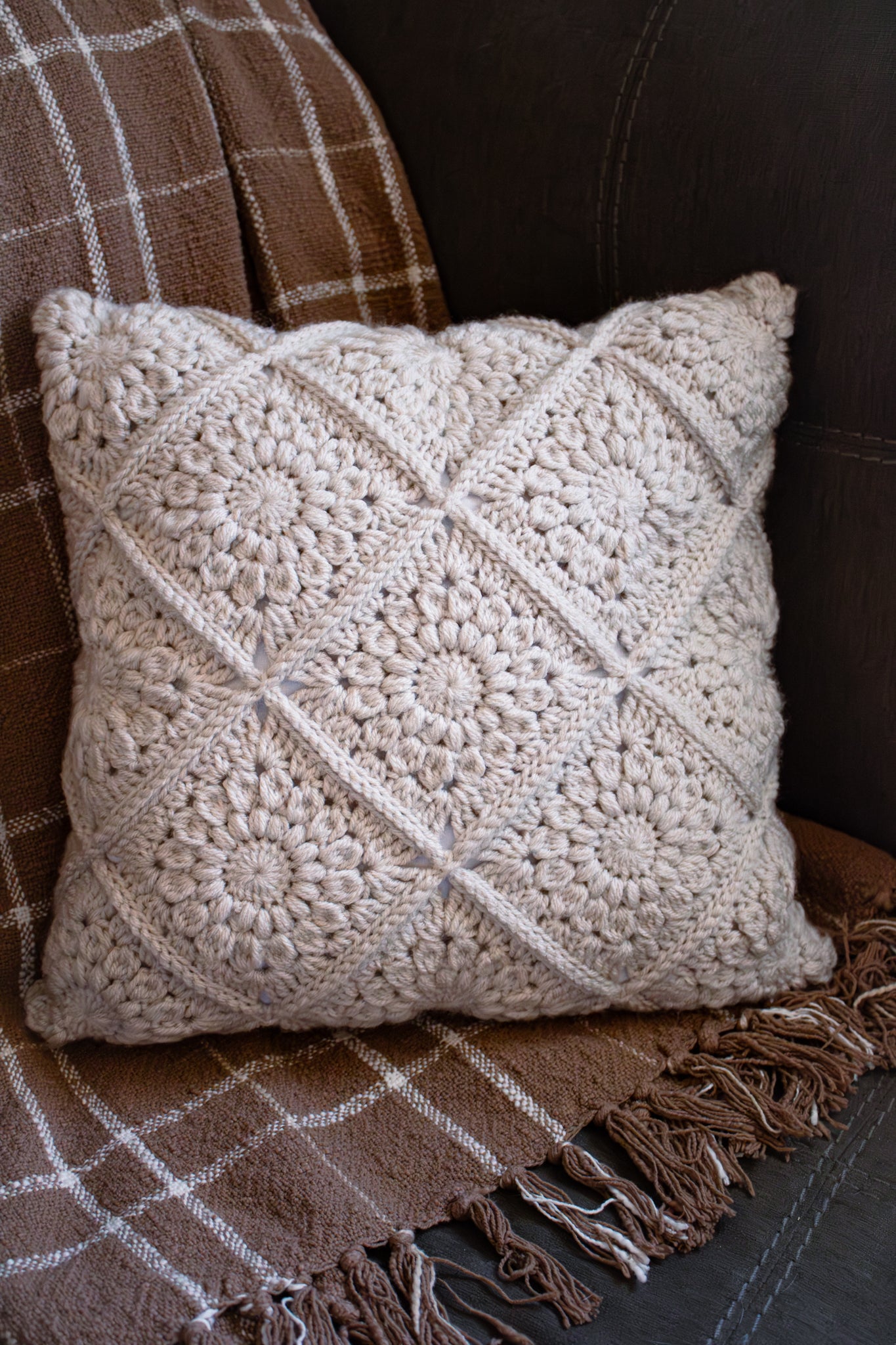 Crocheted pillow on a grey couch and neutral blanket
