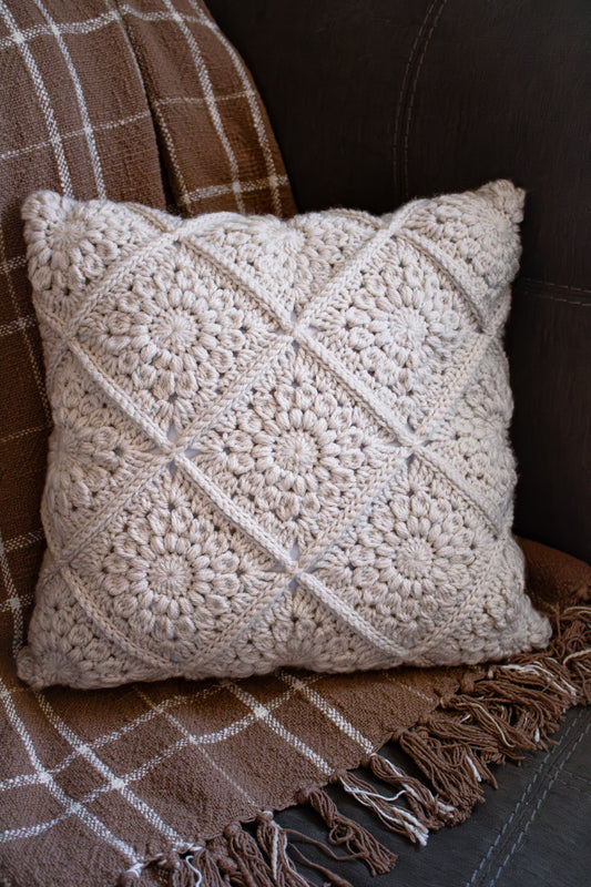 Crocheted pillow on a grey couch and neutral blanket