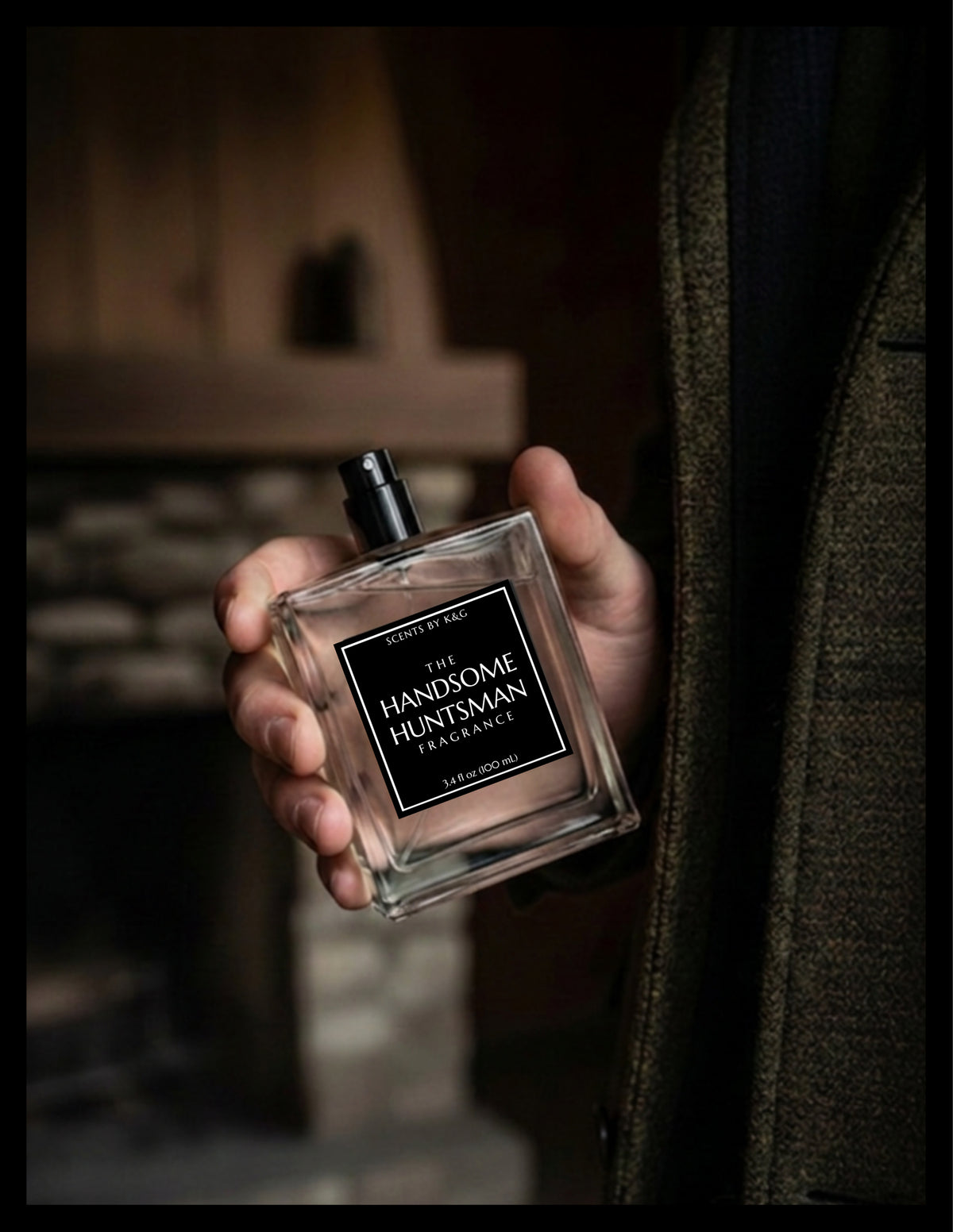 A hand holding a clear glass bottle of 'The Handsome Huntsman' fragrance by Scents by K&G, set against a dark, moody background with a person in a tweed jacket partially visible.