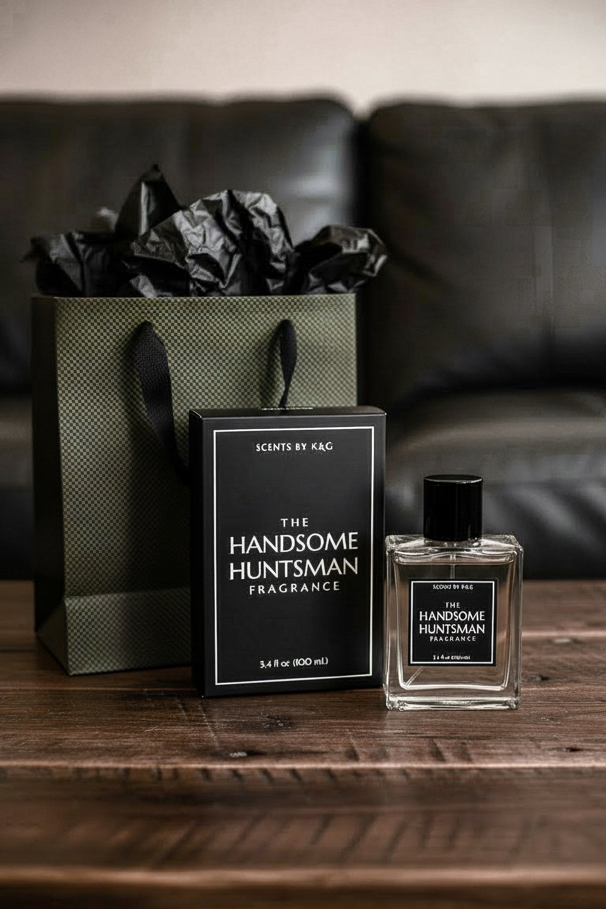 A bottle of 'The Handsome Huntsman" Fragrance next to its gift box and a dark green gift bag on a wood coffee table in front of a dark leather couch.
