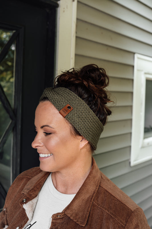 A person wearing an olive green knit headband with visible brand tag.