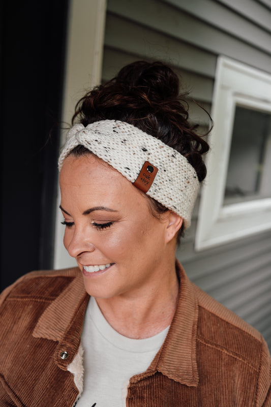 A person wearing an ivory tweed knit headband with brand tag.