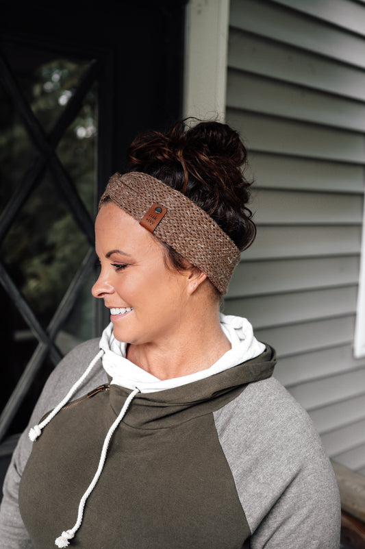 A woman wearing a brown tweed knit headband with visible brand tag.