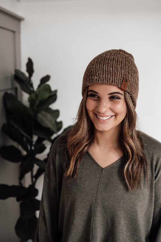 A person wearing a brown tweed beanie with a visible brand tag.