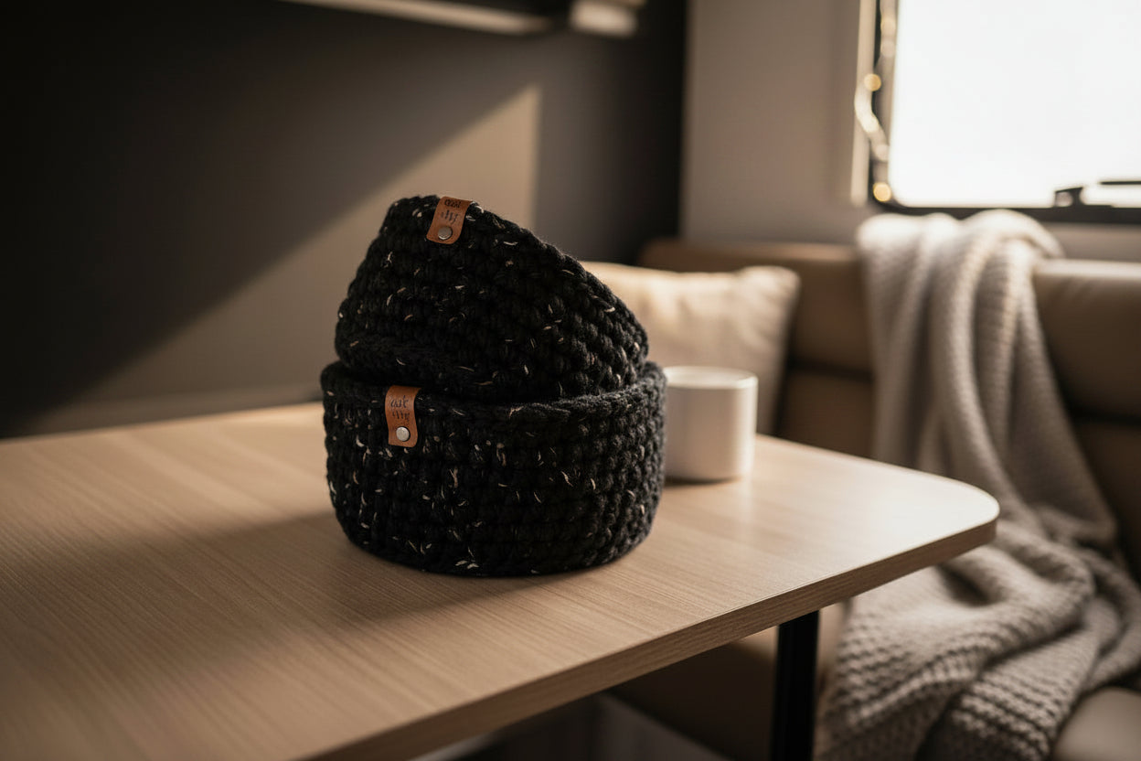 Two nested black crocheted storage baskets with small brown leather brand tags, displayed on a light tabletop in a neutral camper.