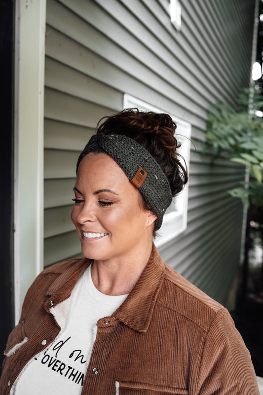 A woman wearing a dark green tweed knit headband with brand tag.