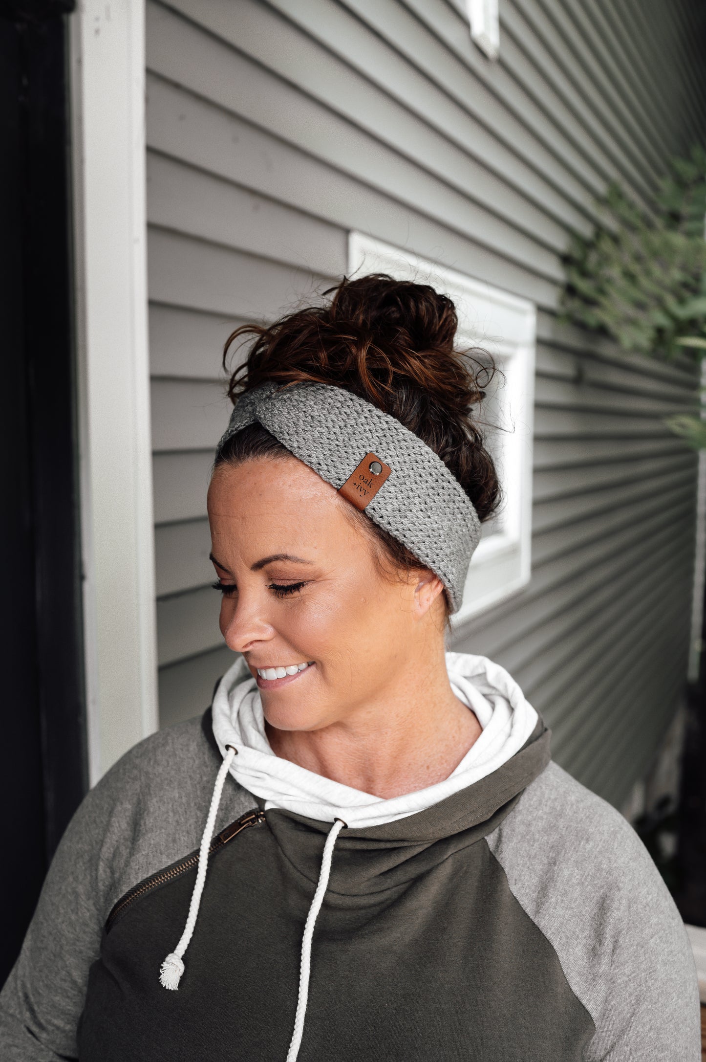 A woman wearing a light grey knit headband with brand tag.