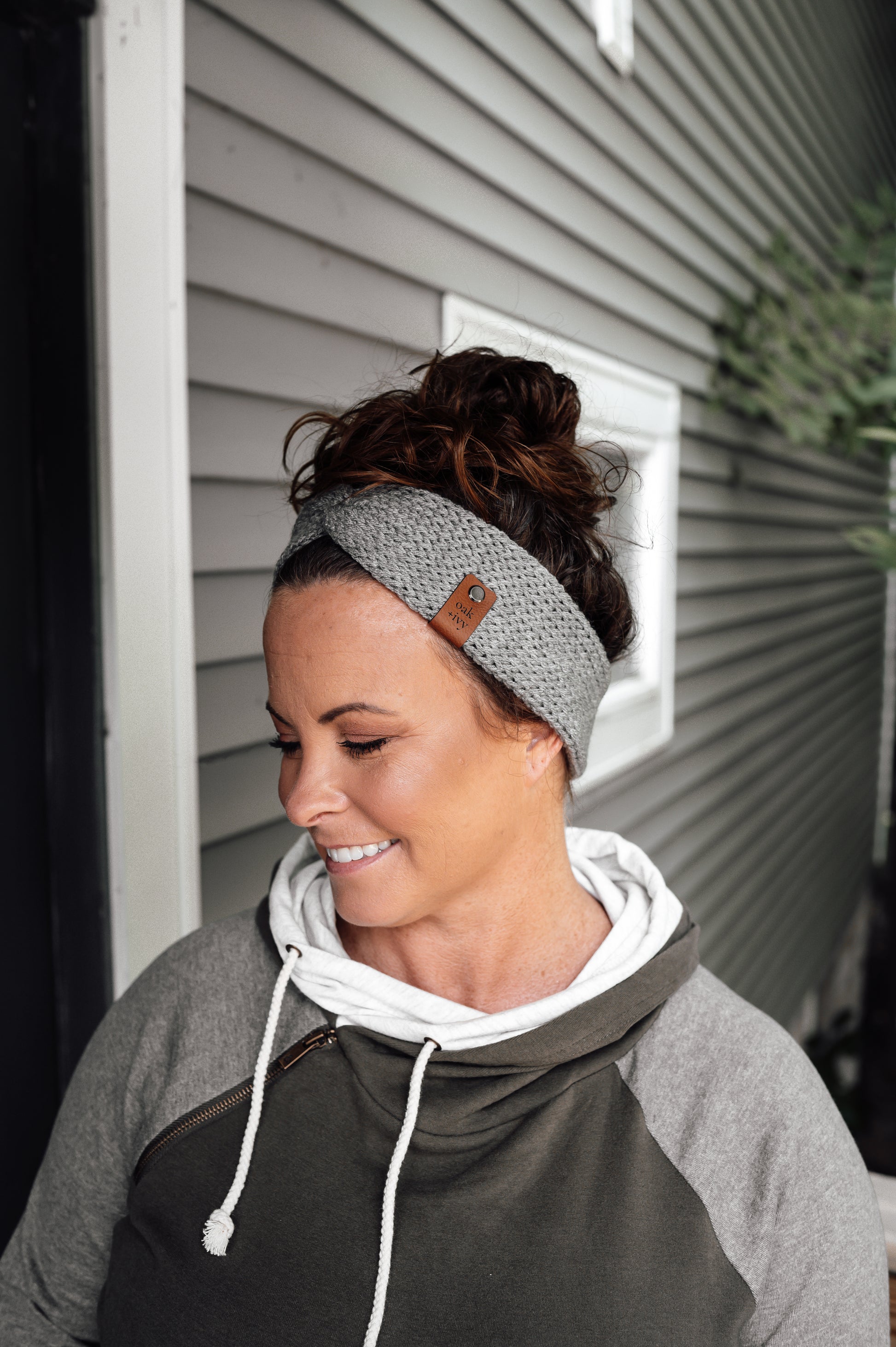 A woman wearing a light grey knit headband with brand tag.