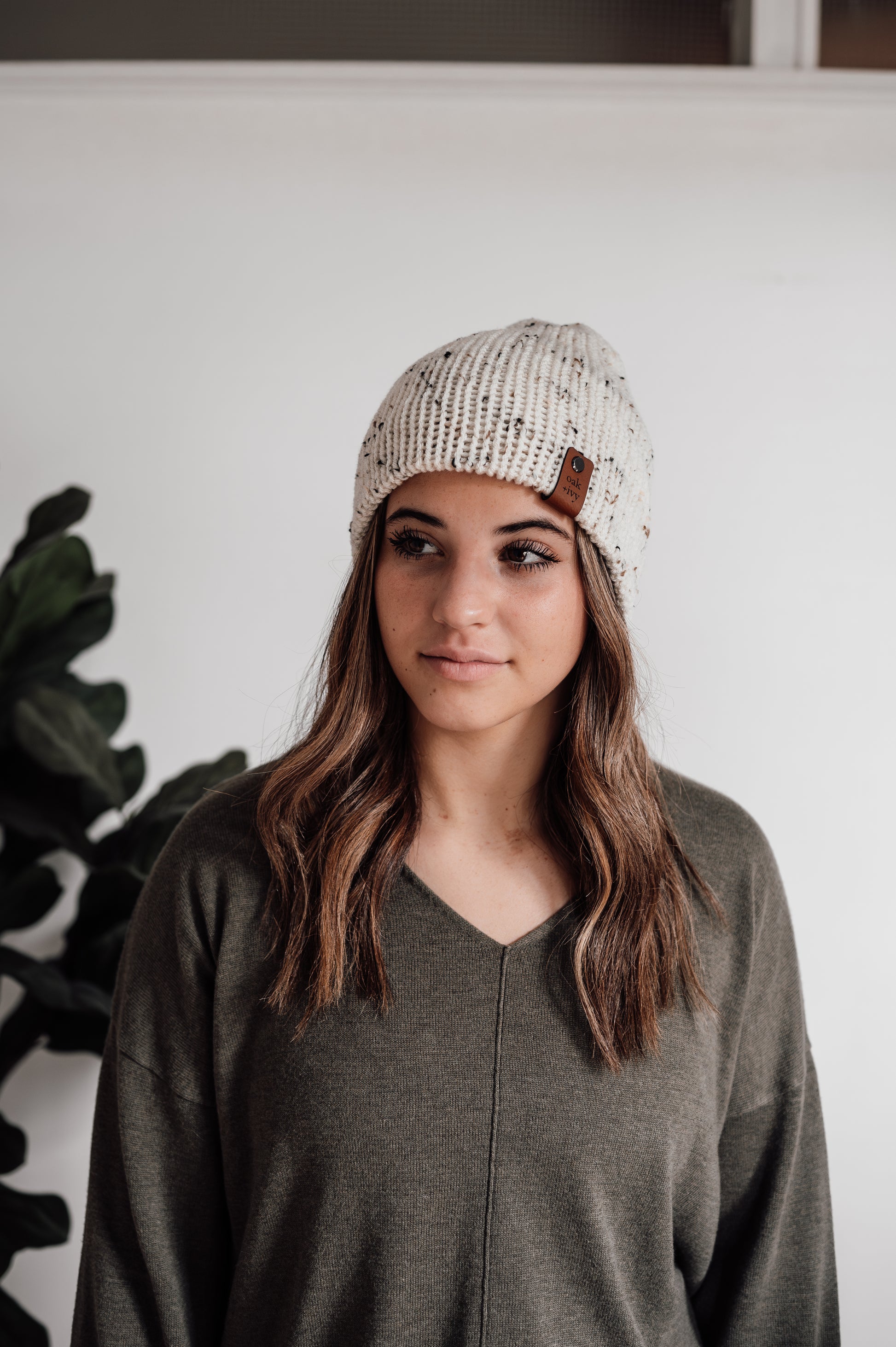 A woman wearing a knit beanie with a tweed pattern in ivory color, standing indoors.