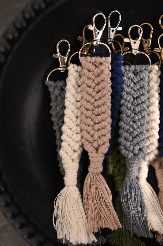 Khaki macrame keychain on top of other braided keychains in a black bowl