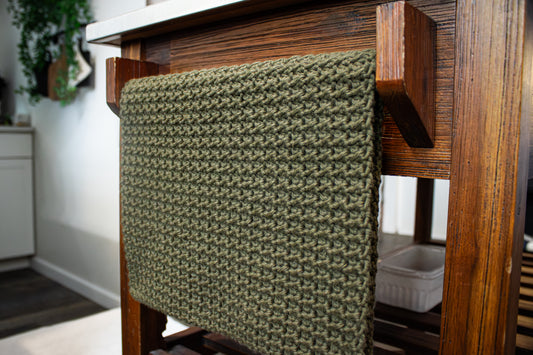 Olive green crocheted towel draped over a towel holder on a kitchen island.