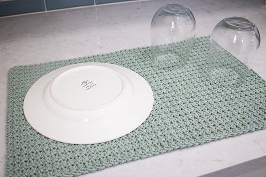 Mint green crocheted towel with a white plate and clear glasses on a marble surface